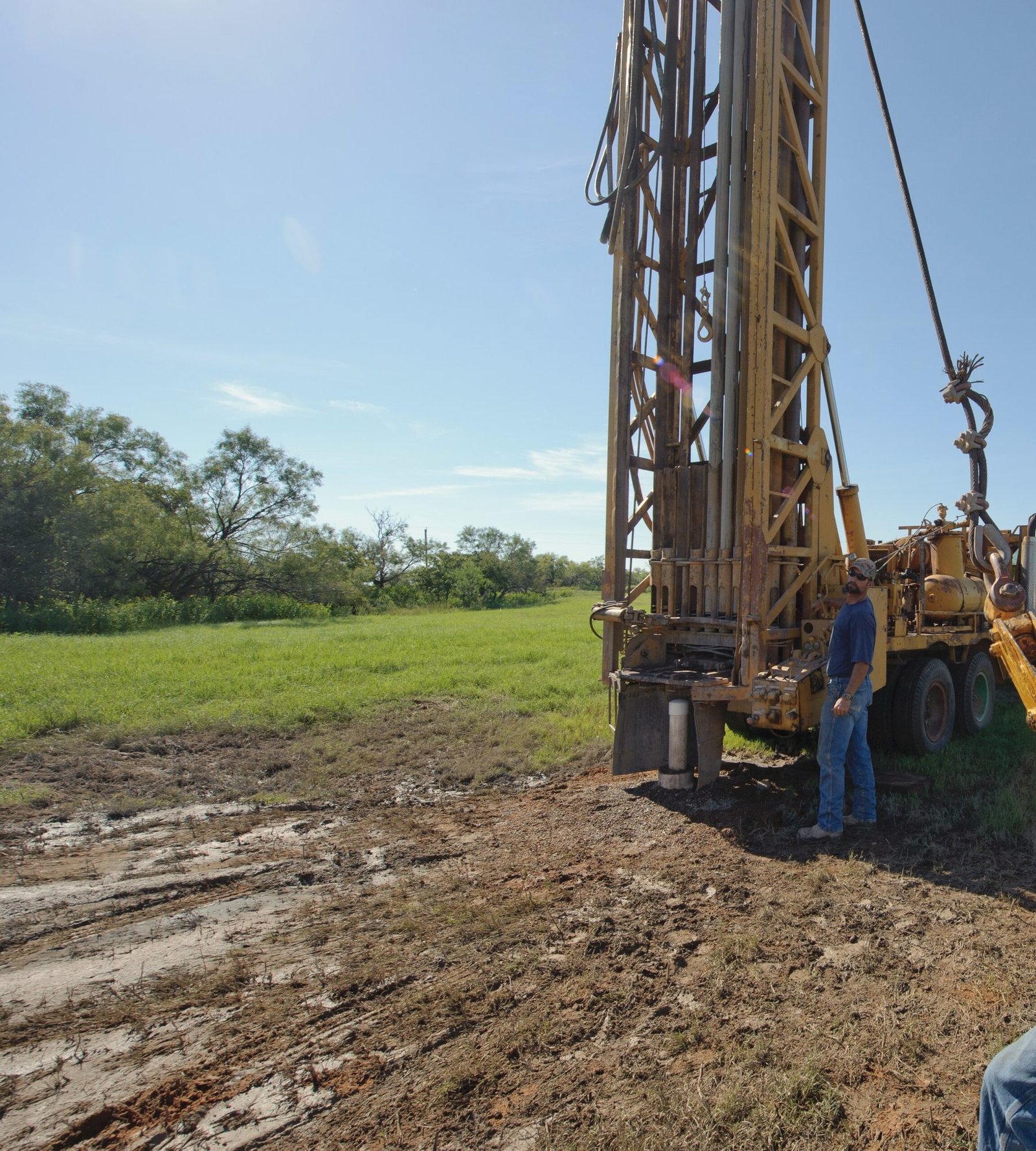 A drilling rig mast raised over a livestock water well in a Texas pasture