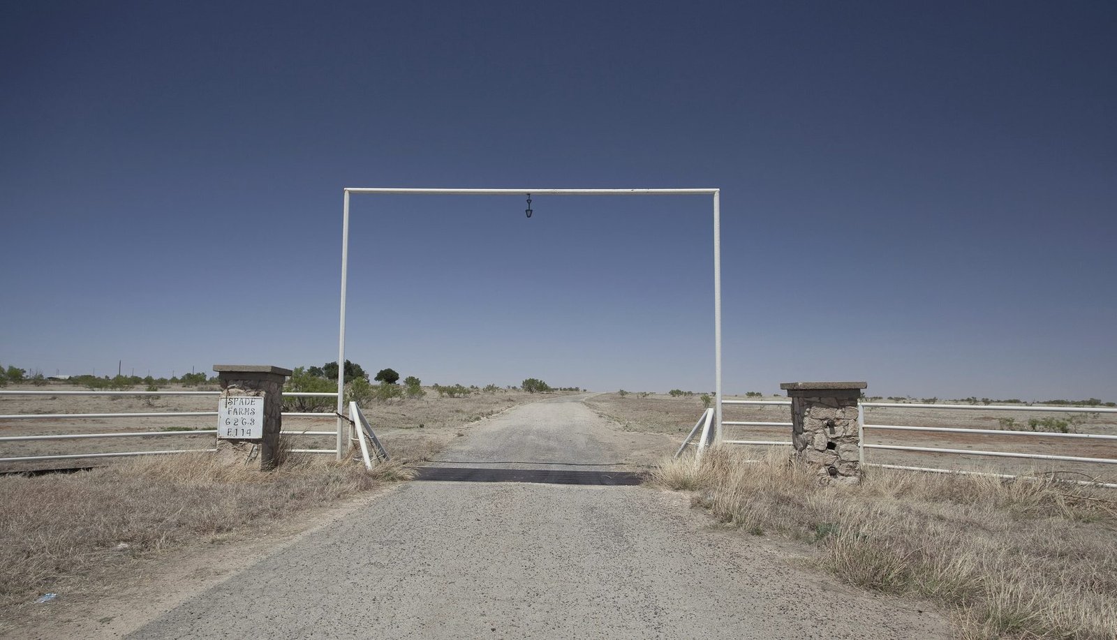 A ranch entrance with a steel gate frame and a cattle guard on a flat, empty road