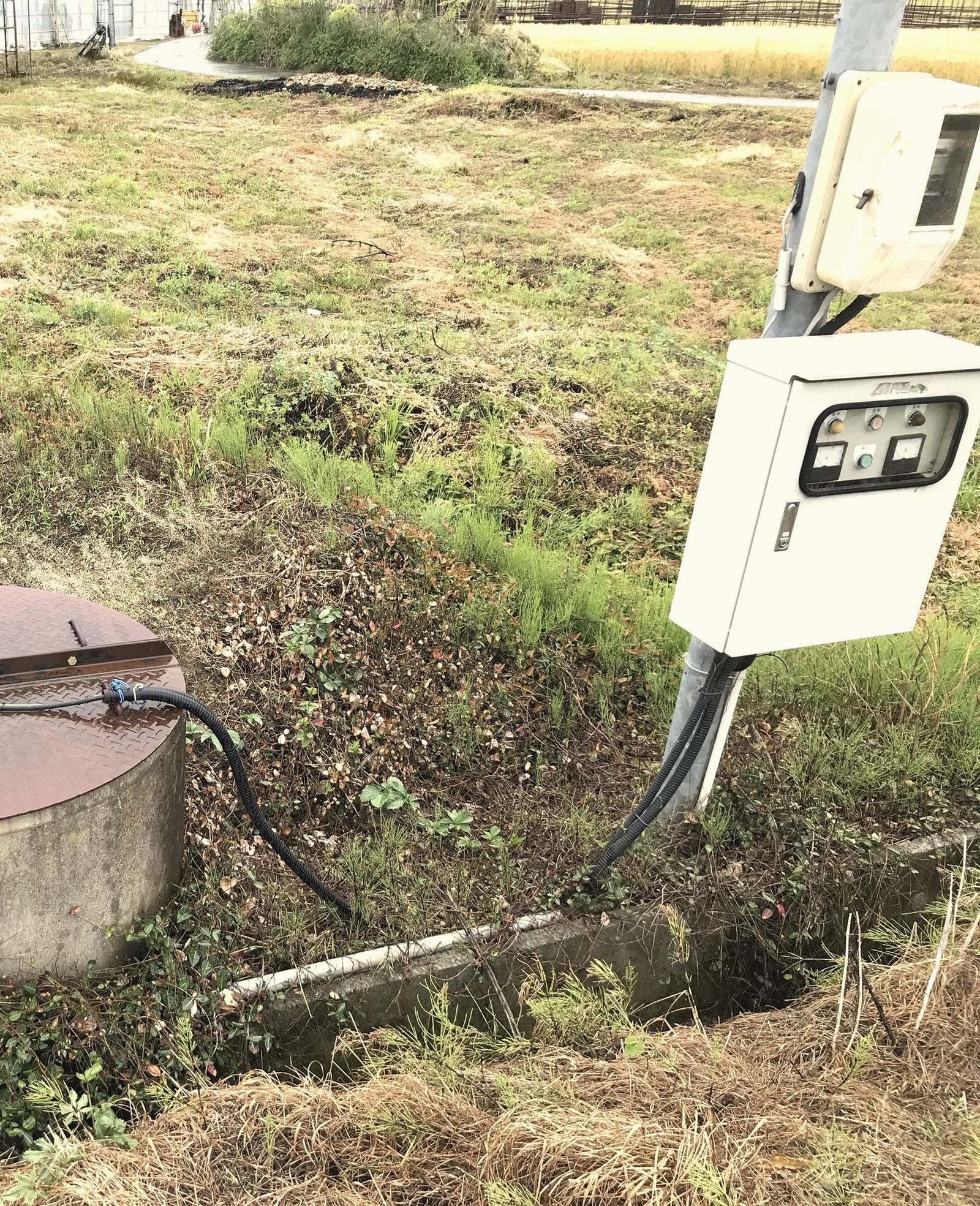 A wellhead with a valve beside a pump control box mounted on a post