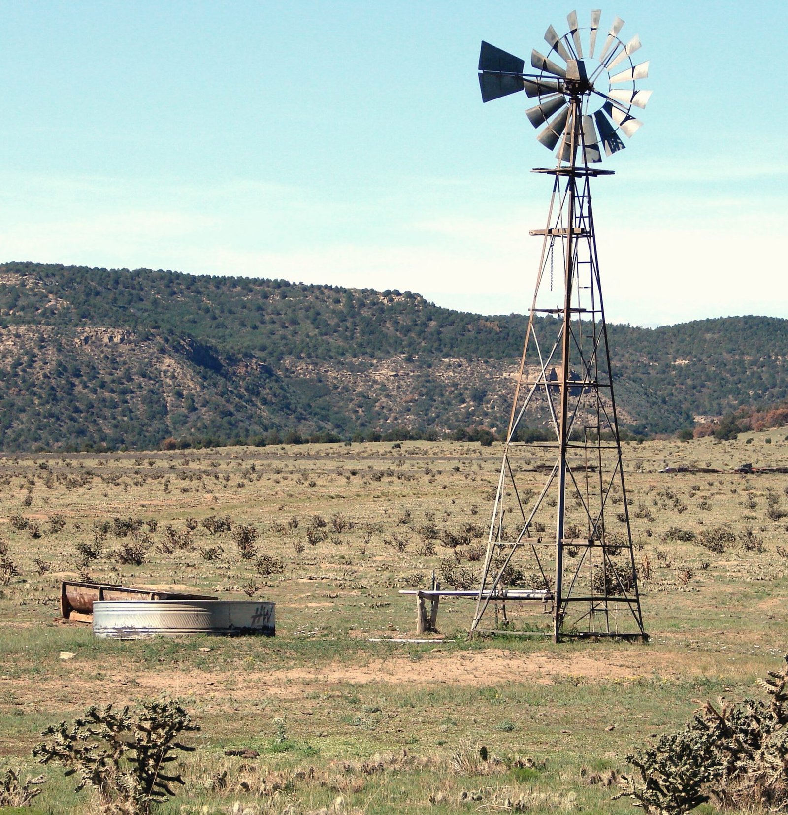 A windmill and a stock tank on dry range below a mesa