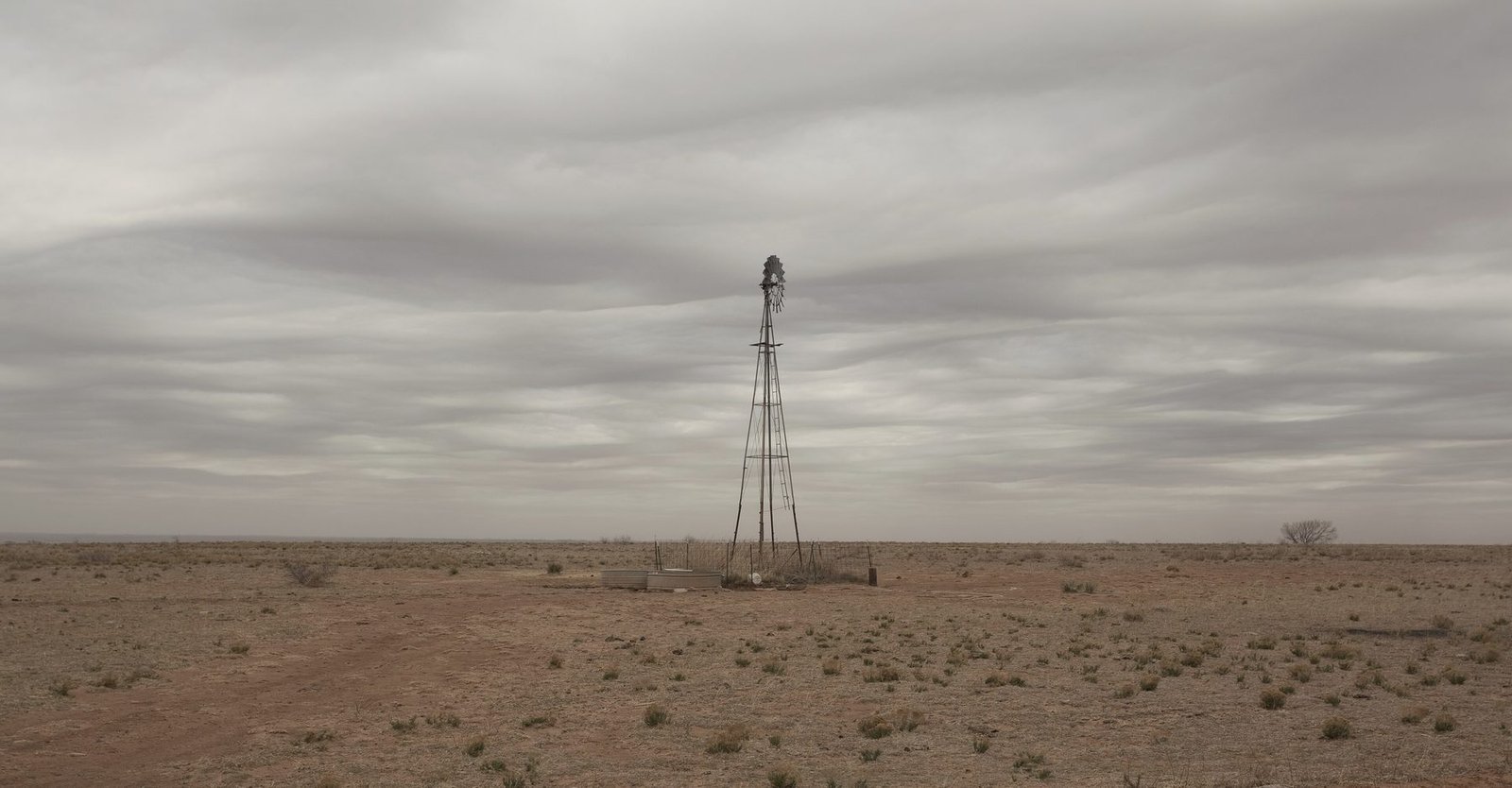 A single windmill on an empty plain under a grey, streaked sky